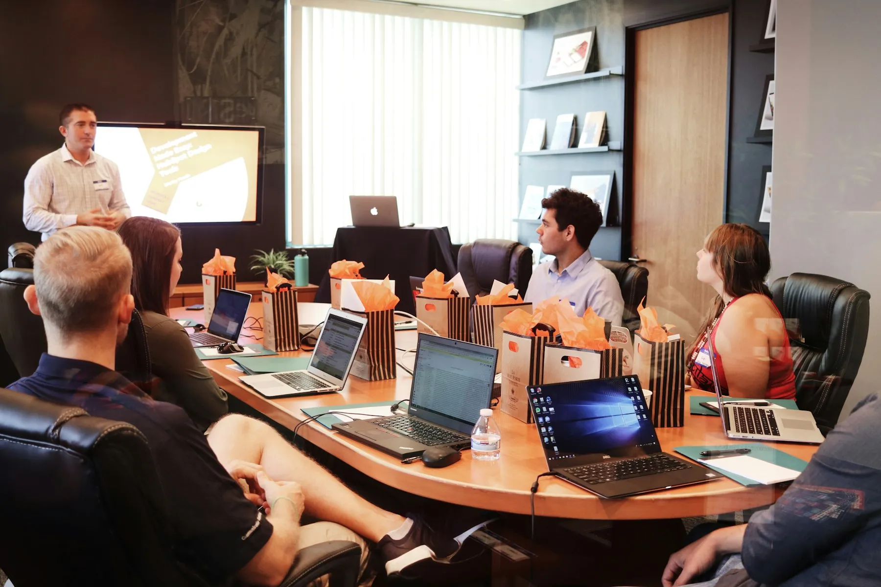 A trainer presenting to a team seated around a meeting table with laptops