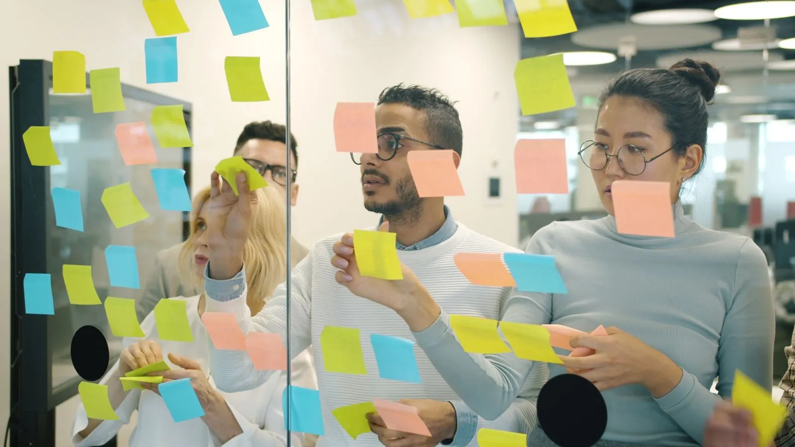A team arranging sticky notes on a glass wall in a workshop